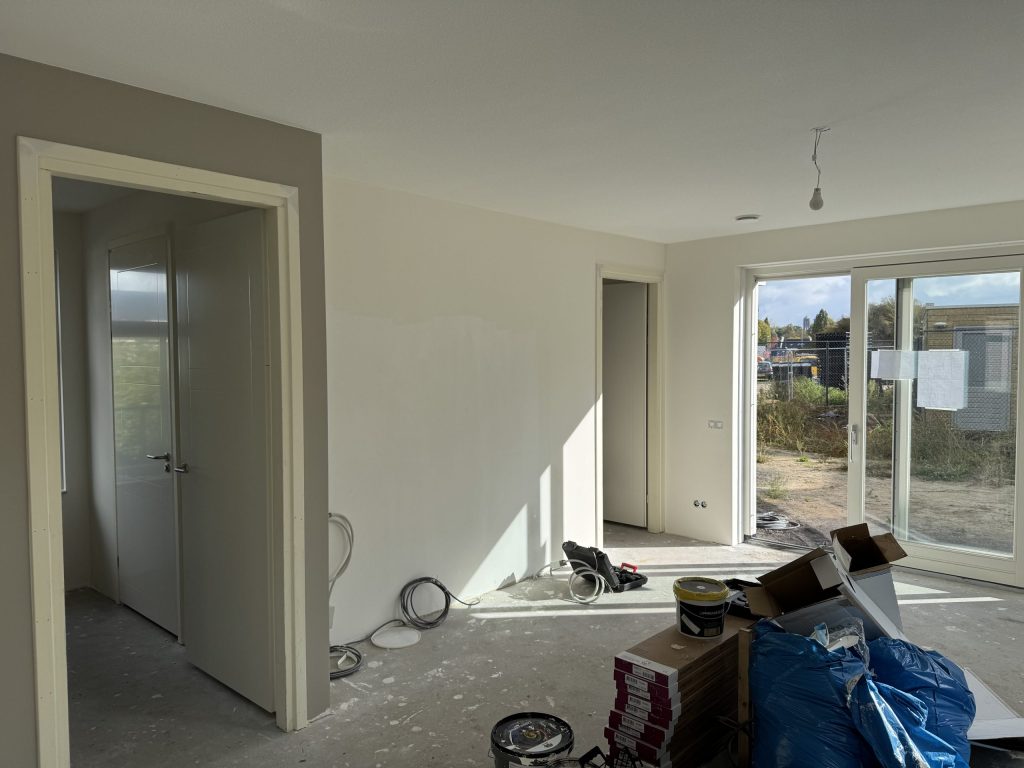 Nieuwbouwwoonkamer halverwege de afwerking met verfemmers, dozen en kabels op de vloer
