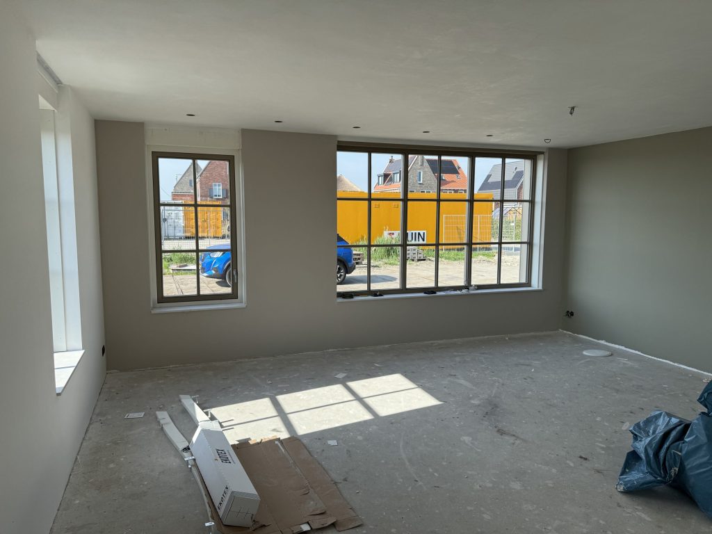Opgeleverde nieuwbouwwoonkamer met strakke grijze wanden, sprossenramen en nog een kale betonvloer