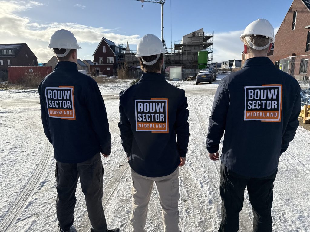 Drie vakmensen van Bouwsector Nederland met witte helm op een besneeuwde nieuwbouwplaats met een bouwkraan